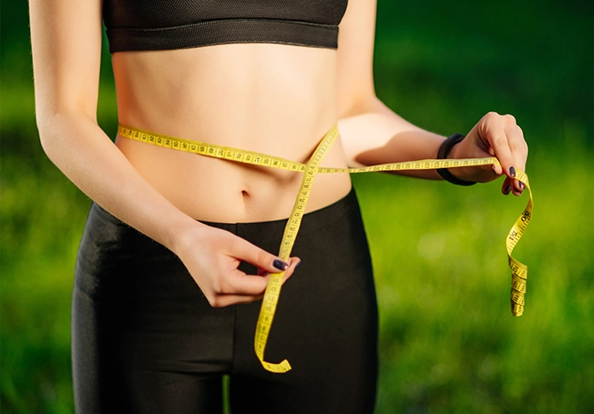 家安生醫｜養生村｜戶外陽光背景下，女性正在測量纖細腰圍，展現健康體態與纖體保健的產品開發成效。